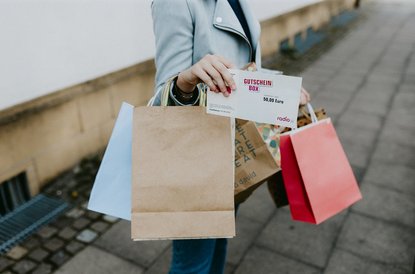 Frau hält viele Taschen in der Hand und einen Gutschein