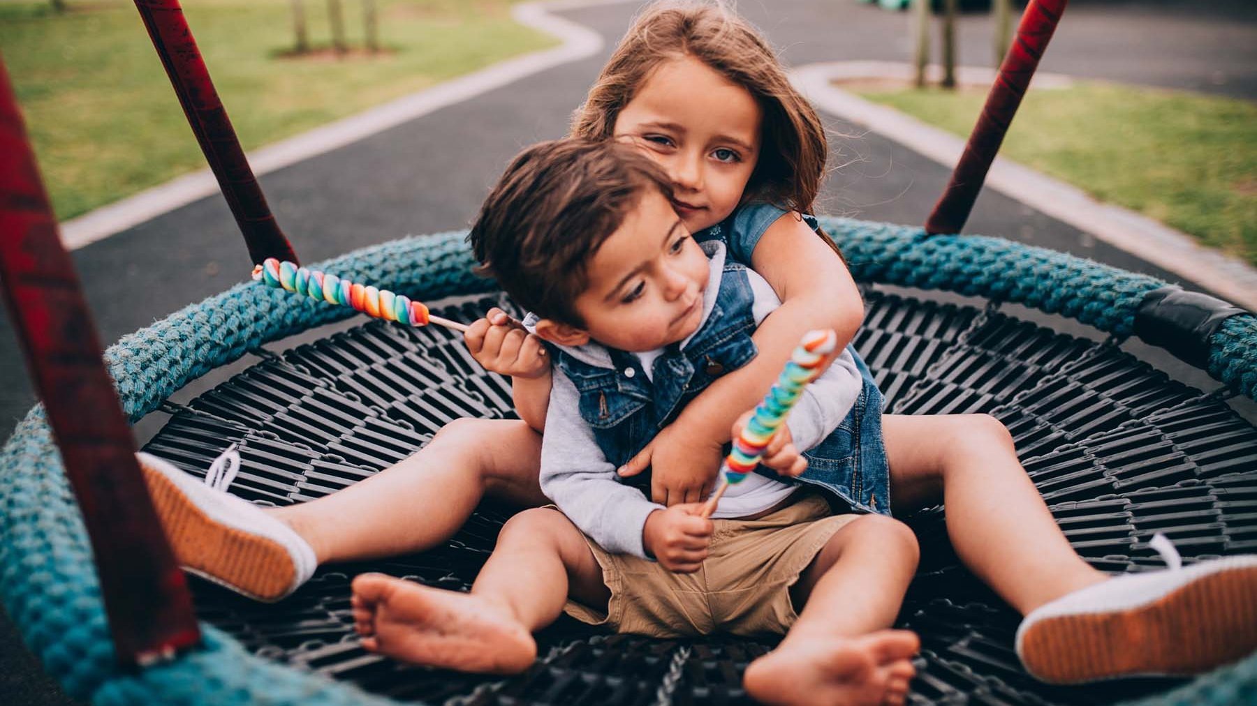 Zwei Kinder sitzen in einer Nestschaukel und halten Lollies.